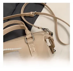 Close-up of shiny silver zipper and logo plaque on a beige patent leather bag
