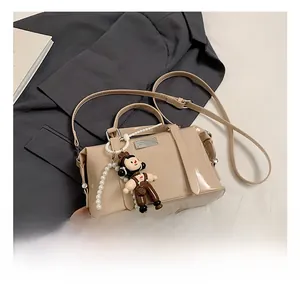Close-up of glossy nude Boston bag featuring pearl chain and cute doll charm detail