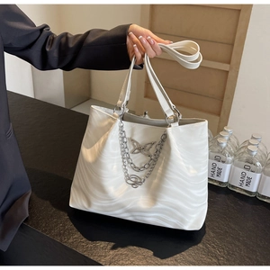 Close-up of white wavy tote bag with silver butterfly charm and metal chain strap detail