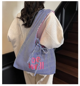 Detailed shot of blue striped canvas tote bag with pink be well lettering and bow drawstrings
