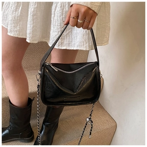 Close-up of black patent leather pillow bag featuring silver chain and wrinkled texture