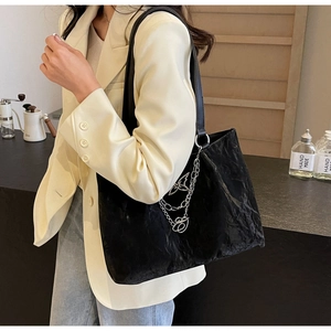 Detail of glossy pleated black tote bag with silver butterfly chain and metal accents
