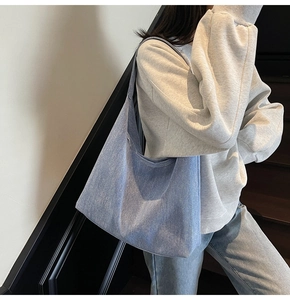 Close-up of light blue denim tote bag texture and wide strap on a model shoulder