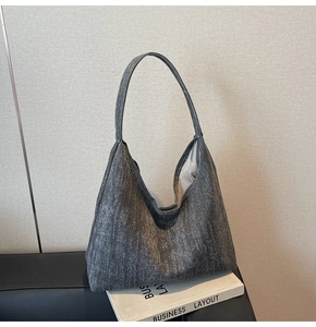 Detail of washed charcoal denim hobo bag placed on a leather sofa with a book