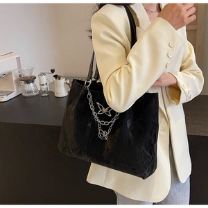 Detail of black wave pattern tote bag featuring a decorative silver butterfly chain charm