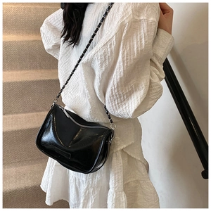 Detail of glossy black pillow bag with silver chain strap on stone stairs