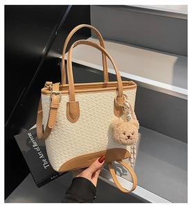 Detail view of woven leather tote bag with brown handles and cute plush bear charm