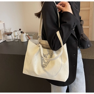 Detailed view of white textured tote bag with silver chain and butterfly charm on shoulder
