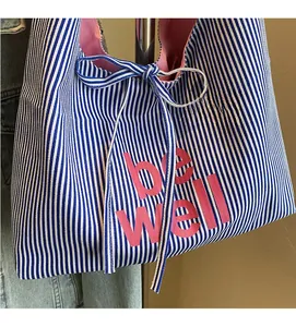 Blue and white striped canvas tote bag detail featuring pink be well text and bow strap
