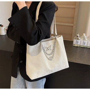 Detail of off-white tote bag featuring wrinkled leather texture and silver butterfly chain