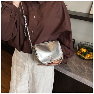 Detail view of silver metallic saddle bag with wrinkled texture and thin chain strap