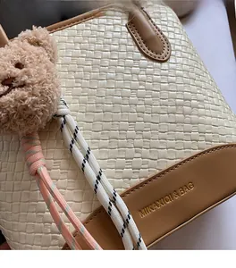Detail shot of the woven texture and golden brand logo on a beige handbag with bear charm
