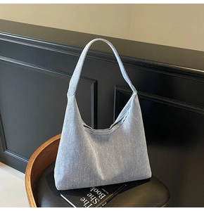 Detail of light blue denim hobo bag texture and wide strap on a leather chair