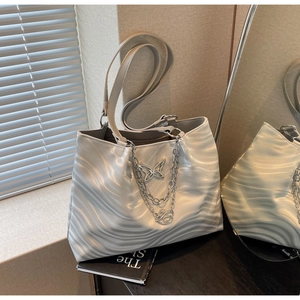 Detail of silver wavy tote bag featuring metallic butterfly charm and chunky chains