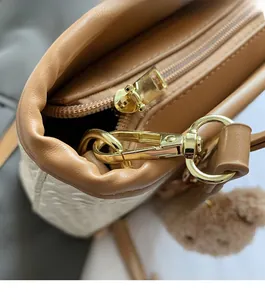 Detail of a brown leather bucket bag with gold hardware and a small plush bear charm