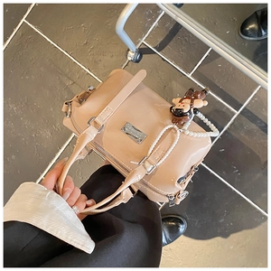 Close-up of beige patent leather Boston bag featuring a monkey charm and pearl chain