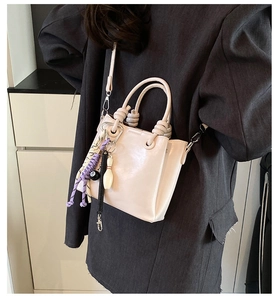 Vue détaillée du sac seau beige sur modèle avec des breloques tendance boule de bowling