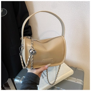 Close-up of beige leather pillow bag with wide handle and silver decorative chain