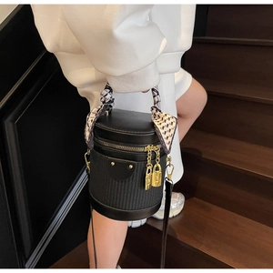 Detail of black cylindrical bag with scarf handle and gold hardware on stairs