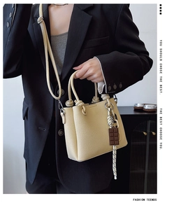 Sac seau beige en cuir grainé avec poignée à nœud présenté sur une veste de costume noire
