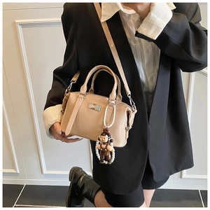 Detail view of a beige Boston bag with a glossy finish and a pearl doll charm