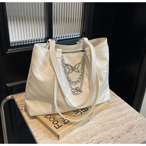 Detail of white wave pattern tote bag featuring silver butterfly metal chain decoration