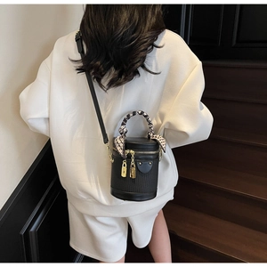 Detail of a black cylinder bucket bag with a silk scarf handle and gold buckles