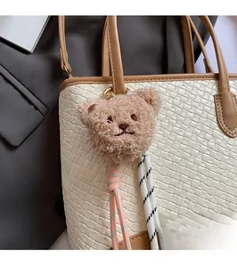 Close-up of a plush light brown bear charm on a woven tote bag for commuters