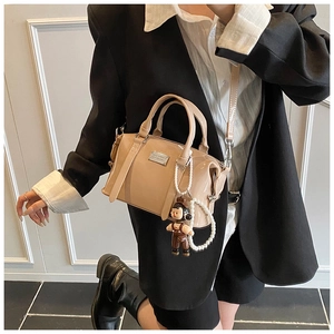 Detail of glossy beige Boston bag with pearl chain and cute doll charm on a model
