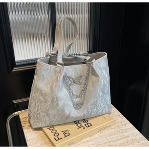Close-up of wave textured tote bag with butterfly charm and layered metal chains