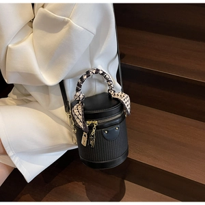 Detailed close-up of black cylinder bucket bag featuring woven texture and scarf handle