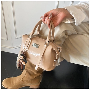 Close-up of glossy beige patent leather Boston bag with pearl chain and metal zipper