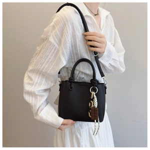 Détail du sac à main en cuir synthétique noir grainé avec un pendentif chocolat