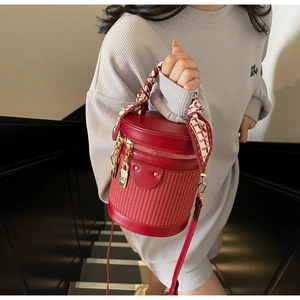Detail of red cylindrical bucket bag with woven texture and scarf-wrapped handle