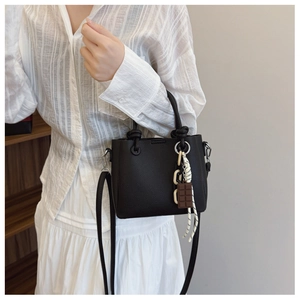 Gros plan d'un sac seau noir en cuir à motif litchi avec poignée nouée et breloques de mode