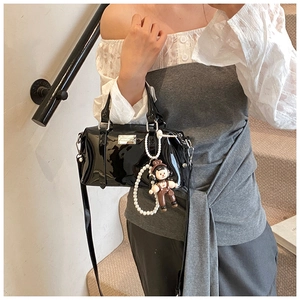 Detail of black patent leather Boston bag with pearl strap and cute doll pendant