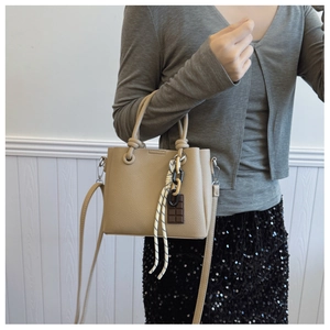 Détail du sac seau beige avec texture litchi, poignées nouées et breloque en chocolat