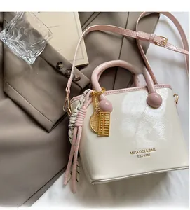 Détail du sac seau en cuir verni crème et rose avec breloques et bandoulière tressée