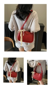 Detail of red leather shoulder bag featuring lace bow and pearl charm ornament
