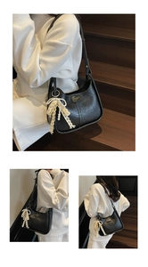Detail of black underarm bag with lace bow, pearl charm, and gold logo plaque