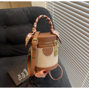 Detail of a brown leather cylinder bag with woven texture and scarf-wrapped top handle