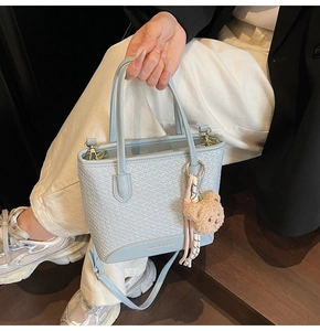 Close-up of light blue woven bucket bag with teddy charm and silk ribbon on stairs
