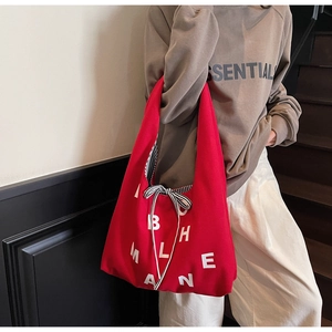 Detail of red canvas tote bag featuring white letters and a black striped bow tie knot