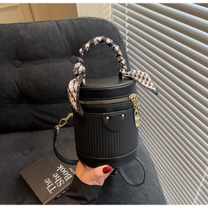 Detail of black cylinder bag featuring woven texture and silk scarf wrapped handle