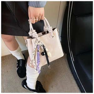 Détail du sac seau en cuir beige avec poignée nouée et breloques colorées de style moderne