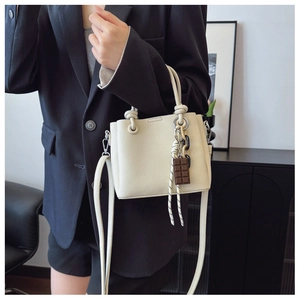 Détail du sac seau blanc cassé avec poignée en corde, texture grainée et breloque chocolat