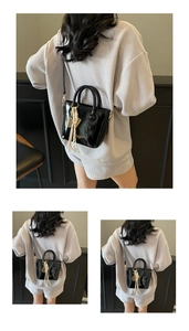 Détail d'un sac seau en cuir verni noir avec un charme de raquette et gland rose
