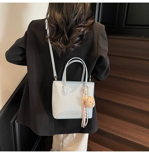 Close-up of light blue woven texture and leather base on women's bucket bag with cute bear charm