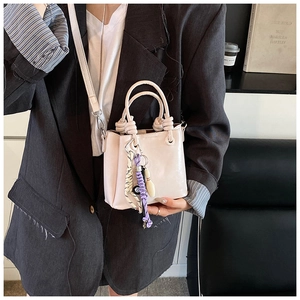 Détail du sac seau beige clair avec breloques porté sur une veste de blazer grise