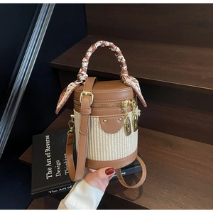 Detailed macro view of a cylindrical bucket bag with woven texture and a silk scarf handle